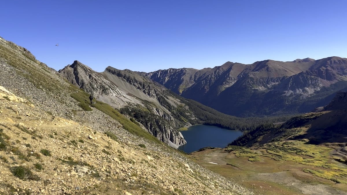 Snowmass Lake in mountain valley with hiking trail view.